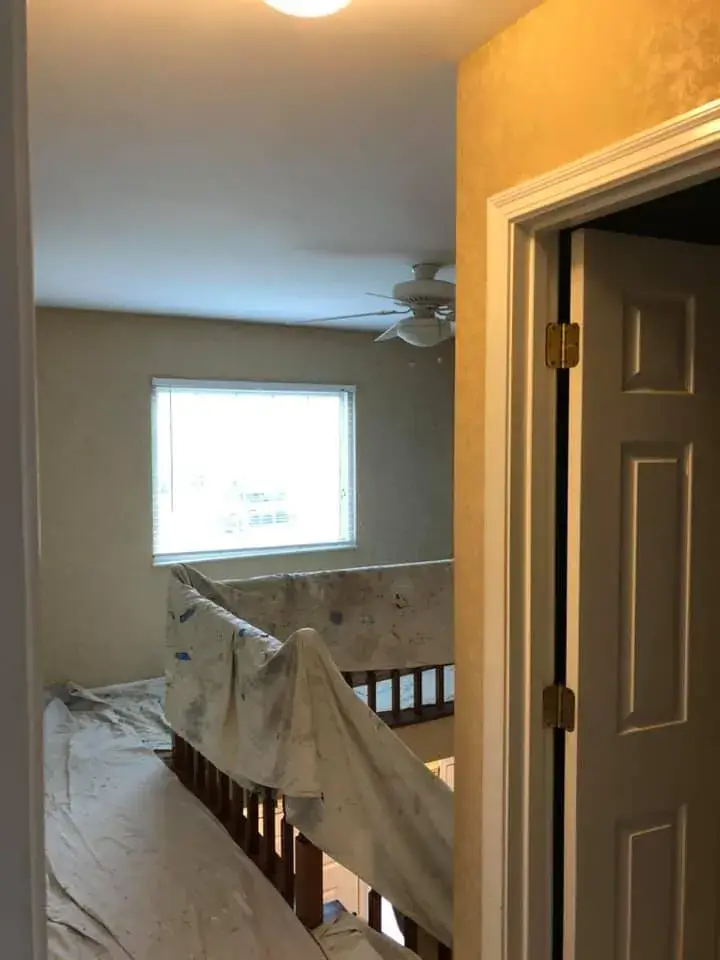 A room interior viewed through a doorway, with drop cloths covering a wooden staircase railing. - My Personal Painter - My Personal Painter In progress: lime green kitchen walls, accent walls, hallway and French doors