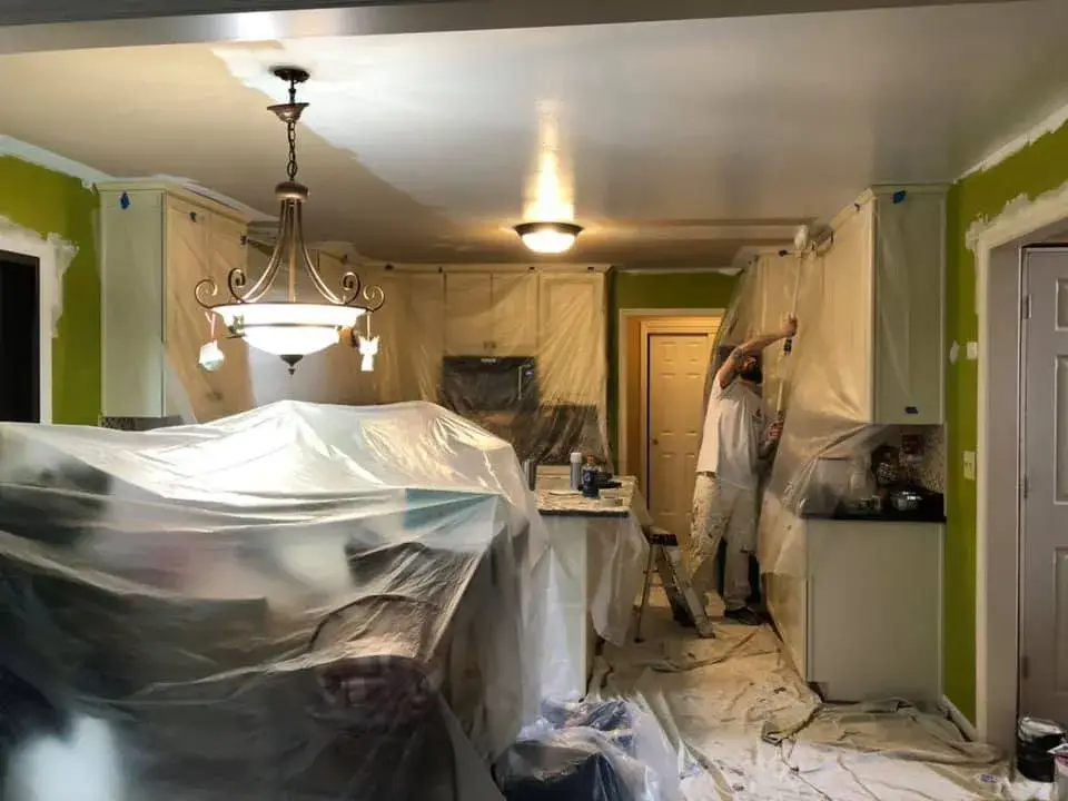 A painter uses a roller to paint kitchen cabinets covered in plastic sheeting. - My Personal Painter - My Personal Painter In progress: lime green kitchen walls, accent walls, hallway and French doors
