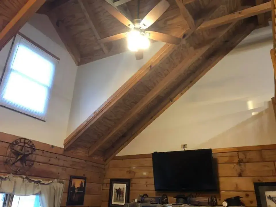 Living room with high wood-beamed ceiling, a ceiling fan, and a wall-mounted television above log walls. - My Personal Painter - My Personal Painter In progress: log home with timber ceilings: walls painted