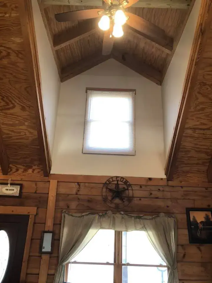 A tall wall in a wood-paneled room featuring a high window with a ceiling fan above and a decorative star below. - My Personal Painter - My Personal Painter In progress: log home with timber ceilings: walls painted