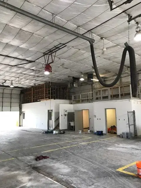Interior of a warehouse with a high, insulated ceiling, industrial lighting, and an office mezzanine. - My Personal Painter - My Personal Painter In progress: metal building interior: walls painted white under insulated fabric ceiling