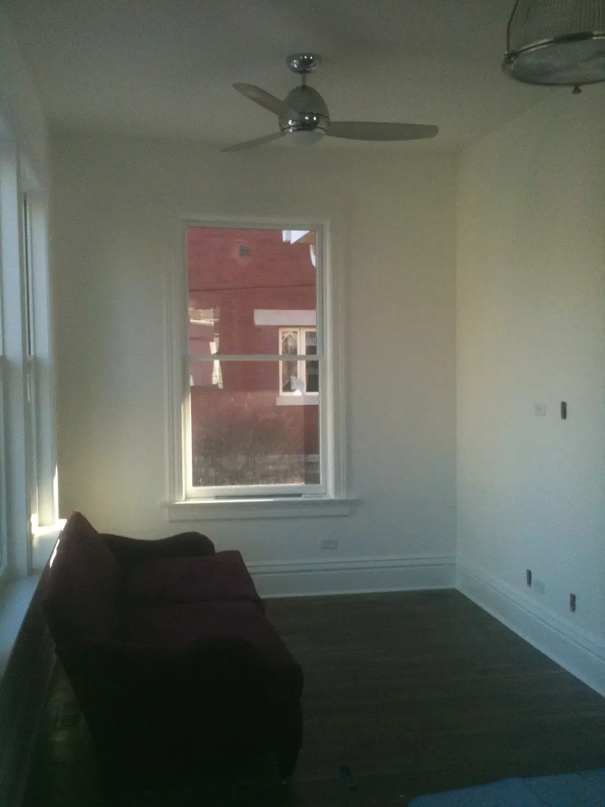 A dark sofa sits in an empty room with a window and a ceiling fan. - My Personal Painter - My Personal Painter After: new-build craftsman house: exterior and interior