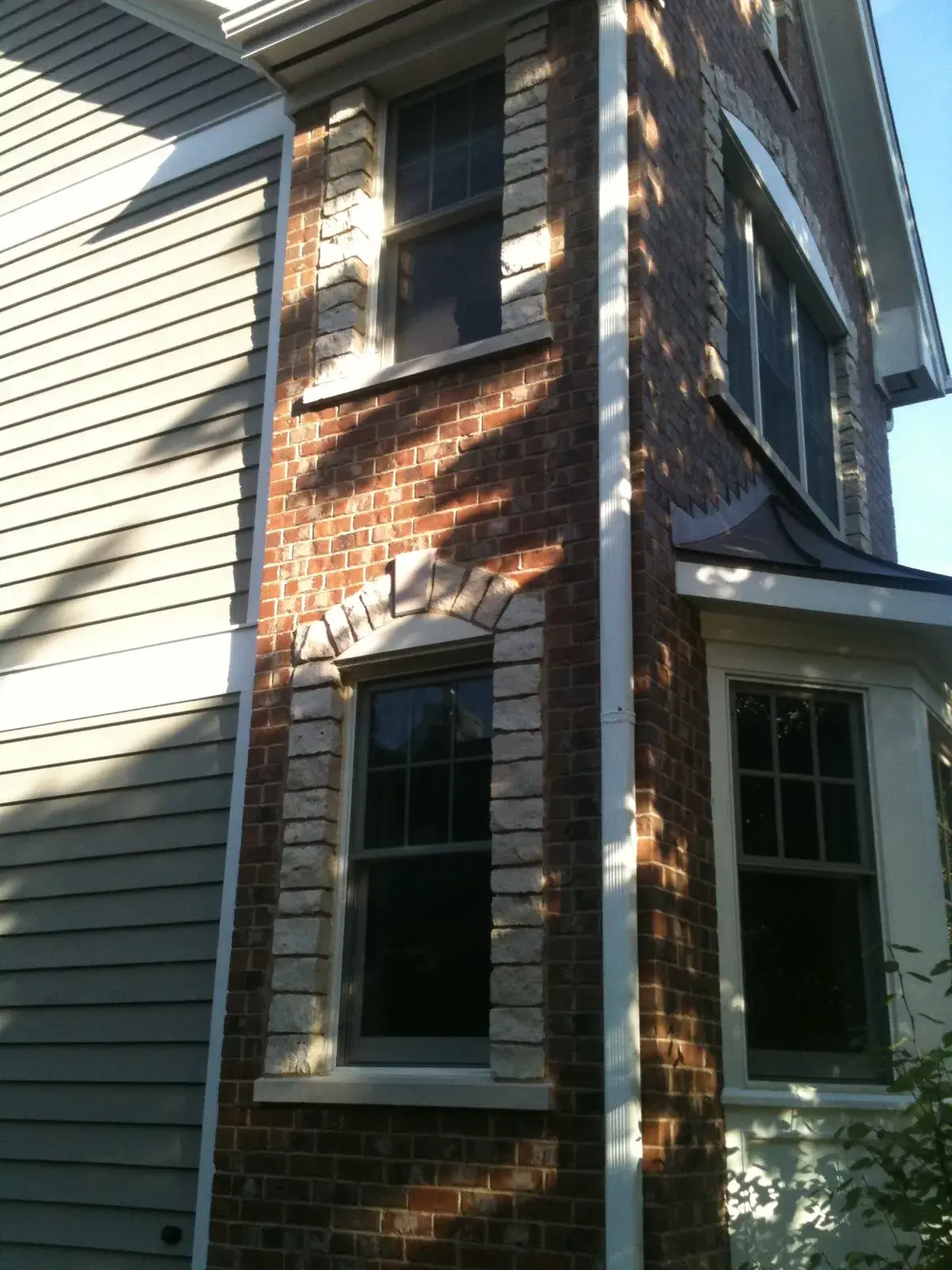 Corner view of a house exterior featuring a brick facade, stone-trimmed windows, and grey siding. - My Personal Painter - My Personal Painter After: new-build craftsman house: exterior and interior