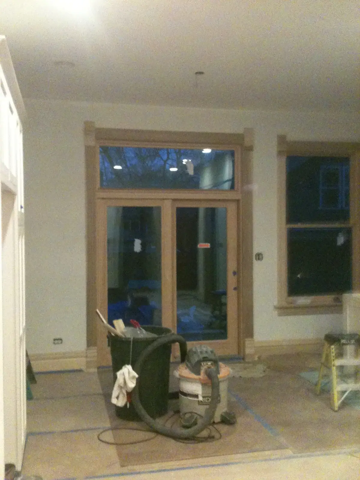 A room under construction with new wooden doors and trim, a trash can, and a shop vacuum on a floor covered in paper. - My Personal Painter - My Personal Painter In progress: new-build craftsman house: exterior and interior