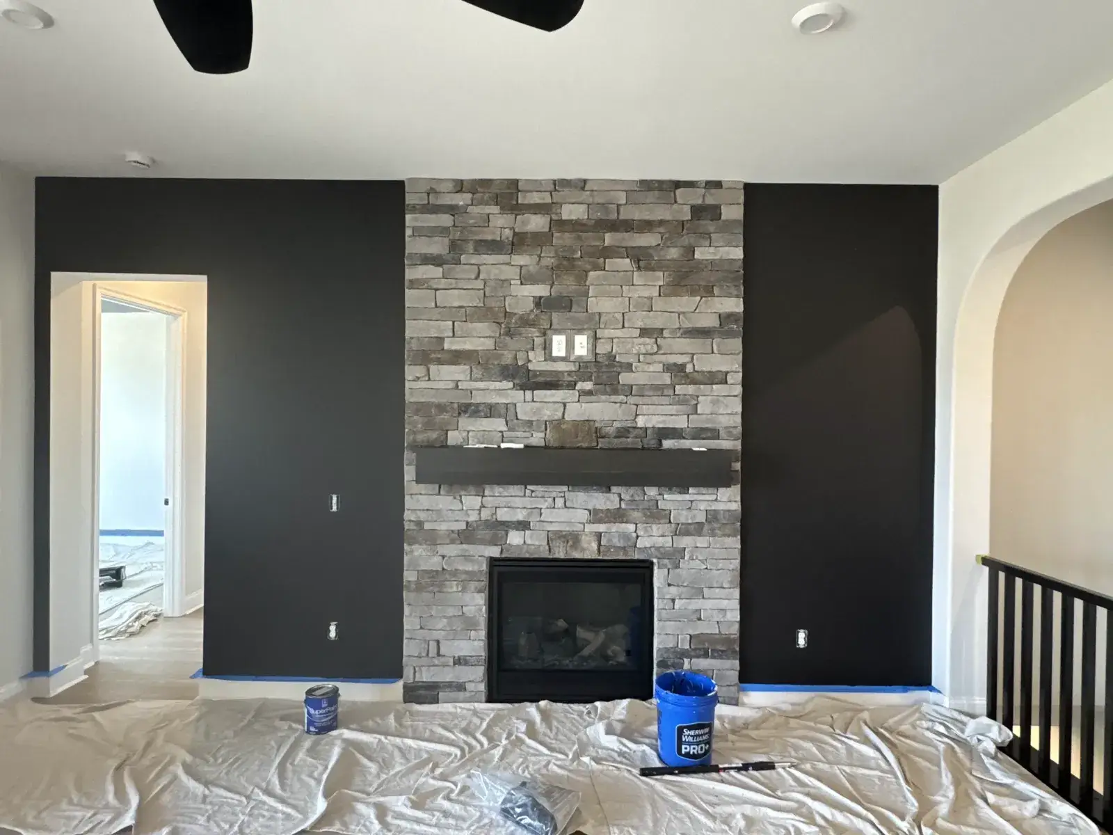 A stone fireplace between two black walls with painting supplies on a drop cloth. - My Personal Painter - My Personal Painter After: new-build house: black archway, accent walls and doors