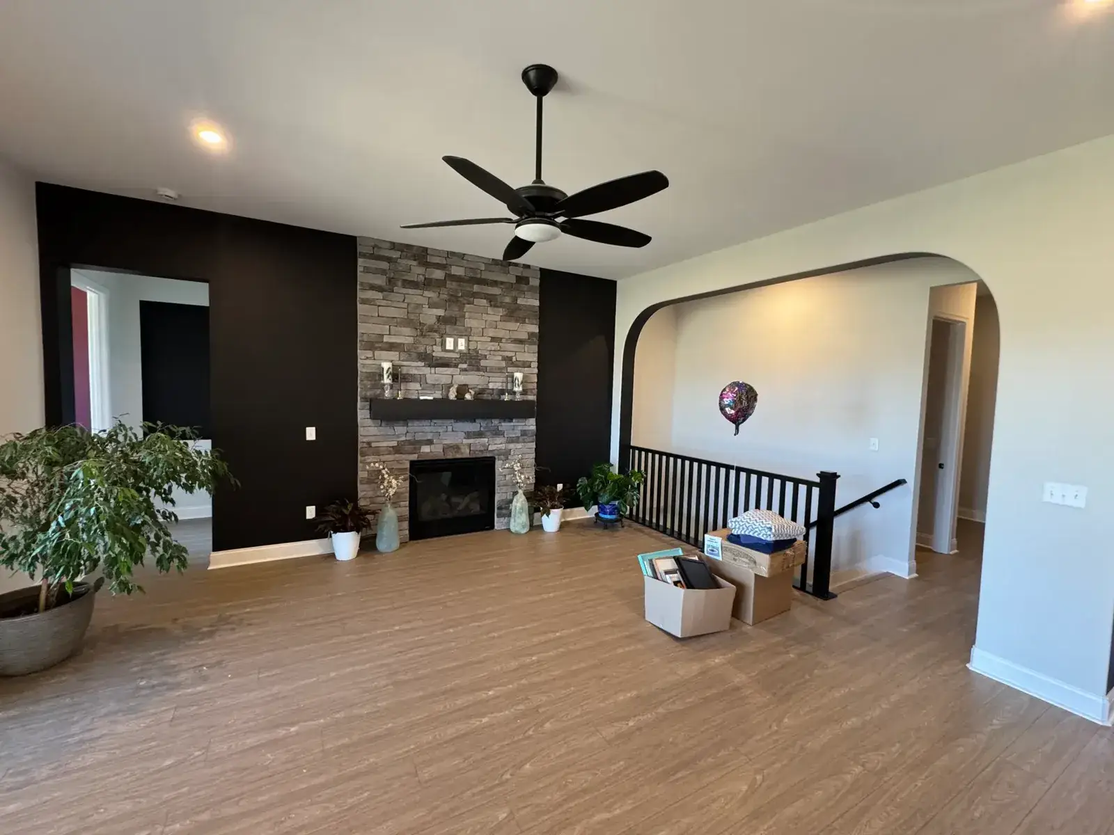 Living room with hardwood floors, a stone fireplace, and moving boxes on the floor. - My Personal Painter - My Personal Painter After: new-build house: black archway, accent walls and doors