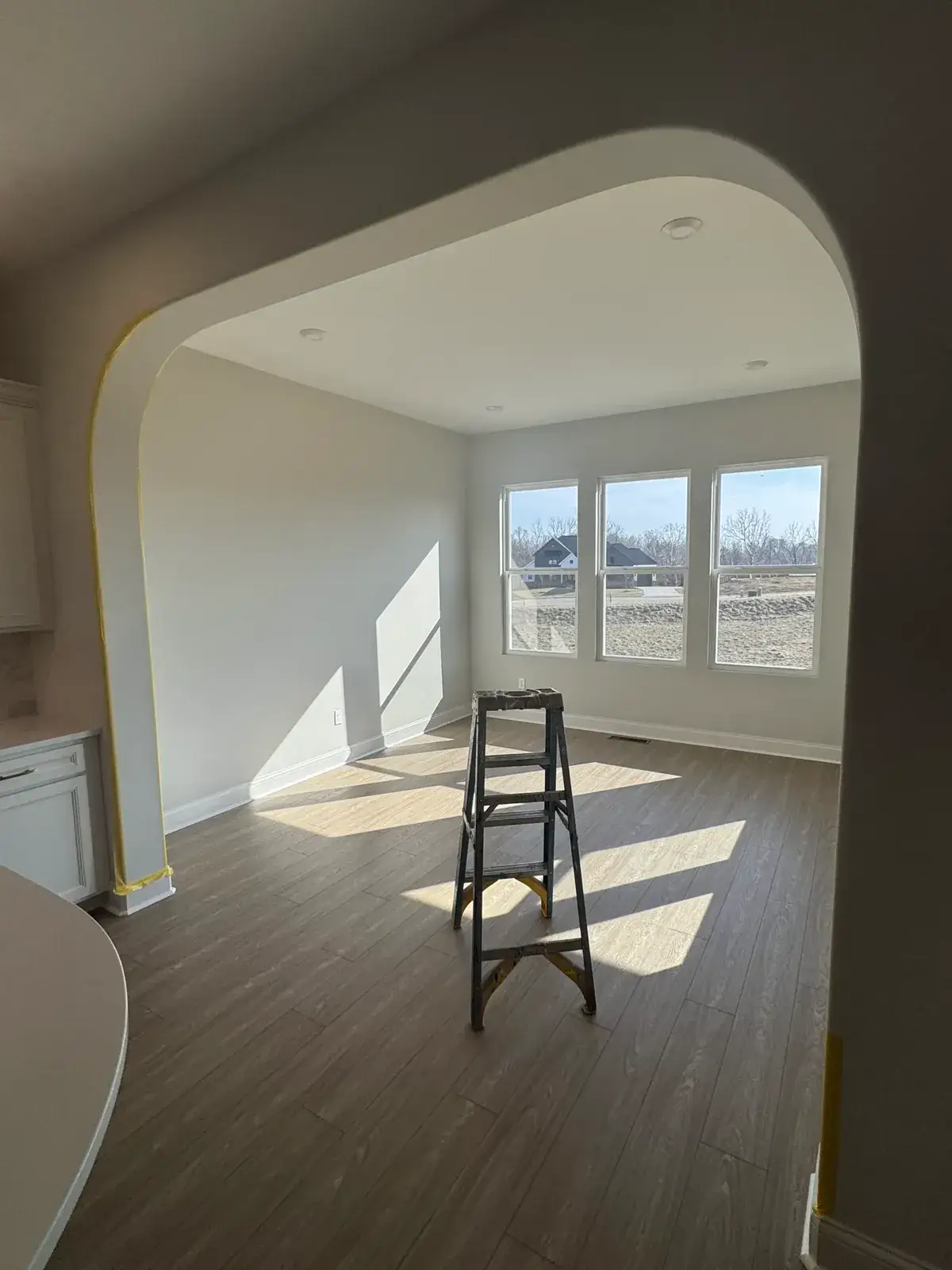 A metal step ladder stands in the center of an empty room with an arched doorway and three windows. - My Personal Painter - My Personal Painter In progress: new-build house: black archway, accent walls and doors