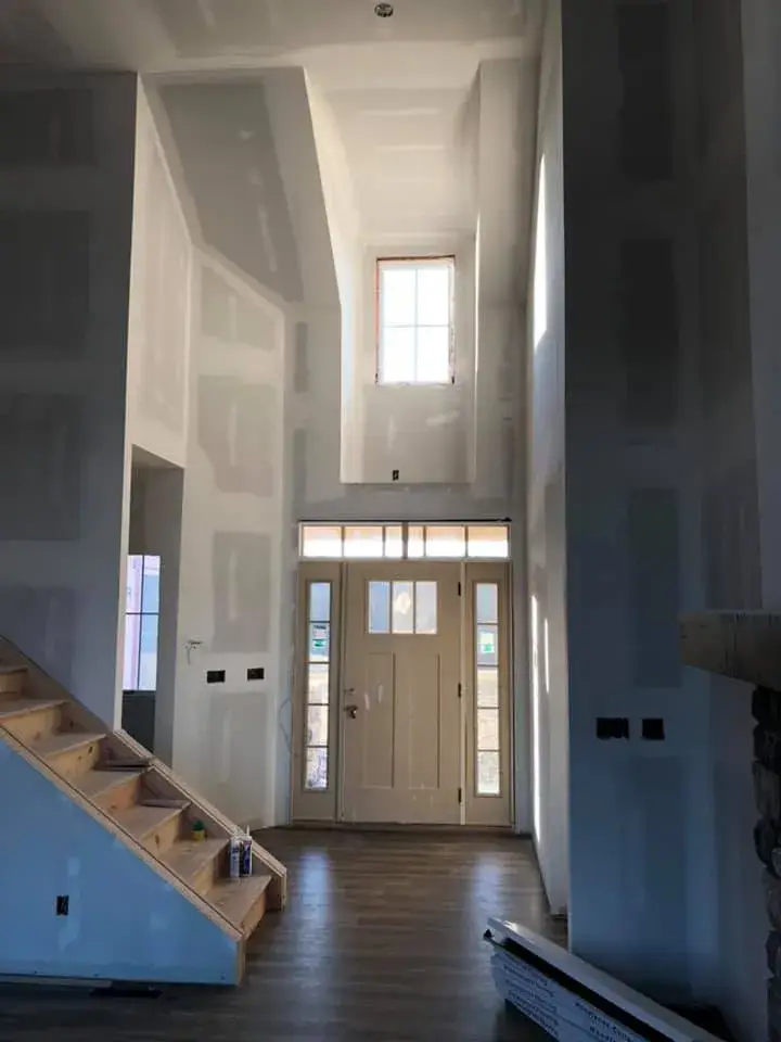 Interior entryway under construction with an unfinished wooden staircase and front door. - My Personal Painter - My Personal Painter Before: new-construction home interior painted