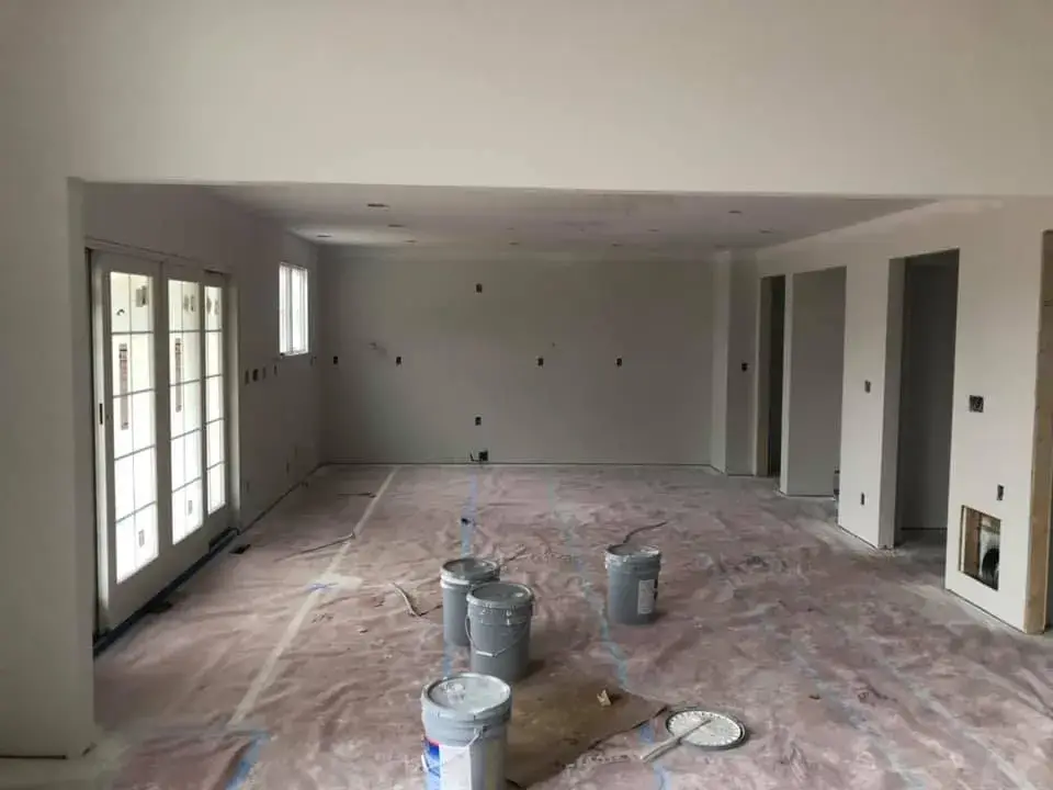 An unfinished room under construction with paint buckets on the floor and protective paper covering the ground. - My Personal Painter - My Personal Painter In progress: new-construction home interior painted
