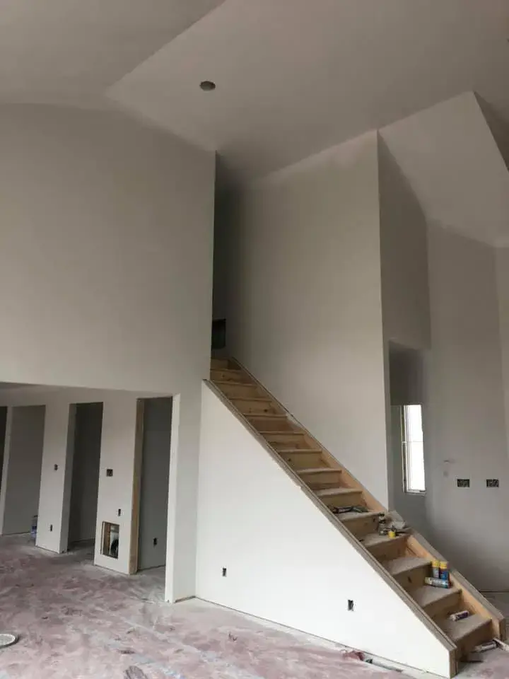 Unfinished wooden staircase inside a room with bare drywall and construction debris on the floor. - My Personal Painter - My Personal Painter In progress: new-construction home interior painted