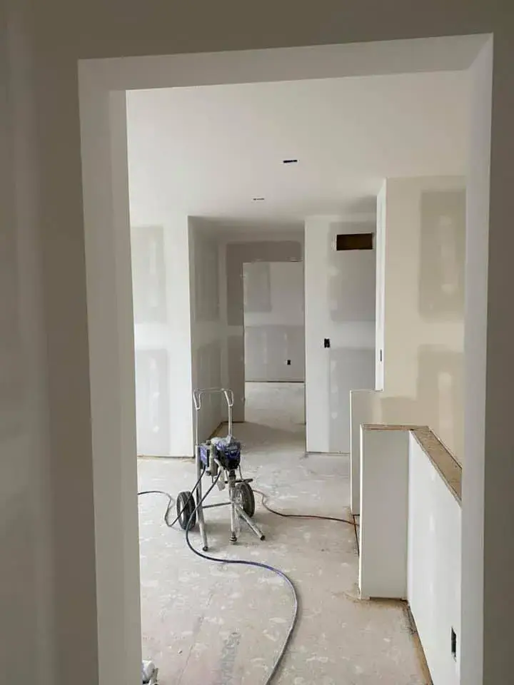 An airless paint sprayer sits on a dusty floor in a room with walls that have been taped and mudded. - My Personal Painter - My Personal Painter In progress: new-construction interior walls painted