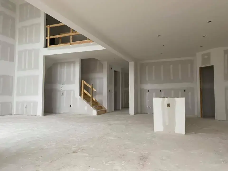 Open floor plan of a house under construction with unfinished drywall, a wooden staircase, and a lofted area. - My Personal Painter - My Personal Painter Before: new-construction interior with open stairwell