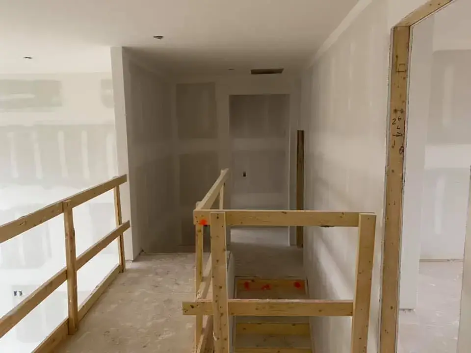 An interior view of a house under construction with unfinished drywall and temporary wooden safety railings on a staircase. - My Personal Painter - My Personal Painter Before: new-construction interior with open stairwell