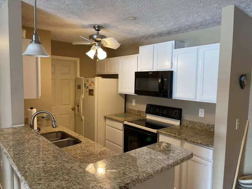 Kitchen with white cabinets, speckled granite countertops, and a black microwave and stove. - My Personal Painter - My Personal Painter After: oak kitchen cabinets painted white
