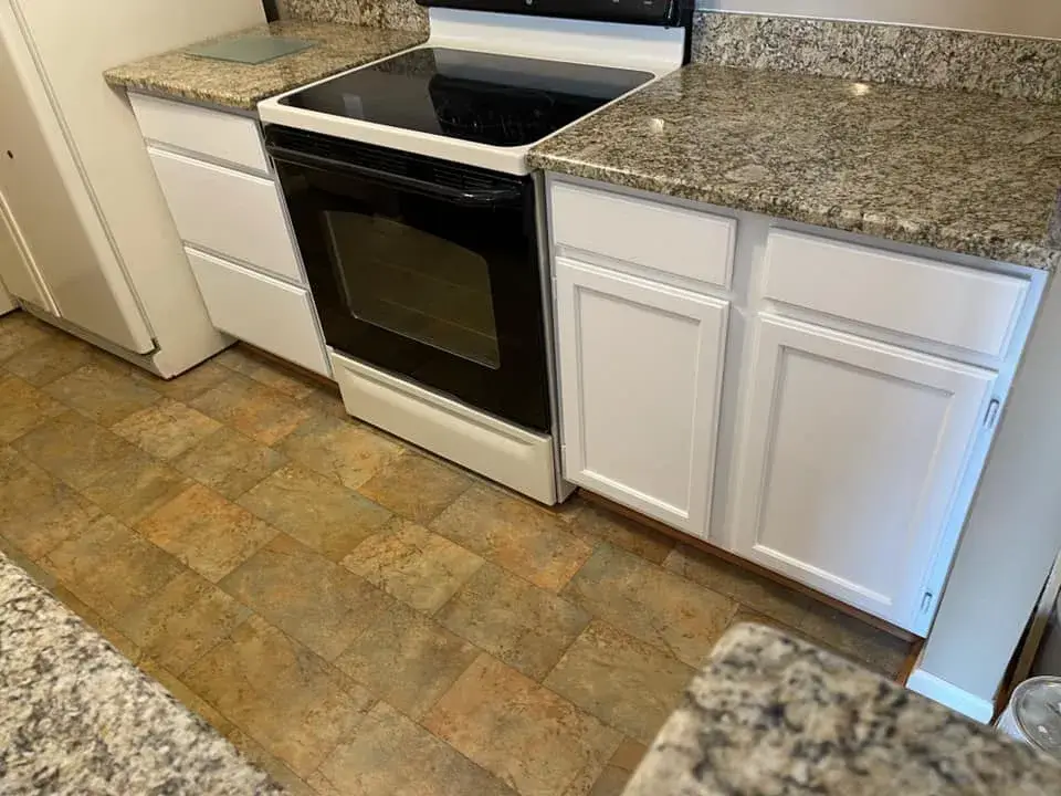 Black electric stove nestled between white cabinets and speckled granite countertops over a tiled floor. - My Personal Painter - My Personal Painter After: oak kitchen cabinets painted white