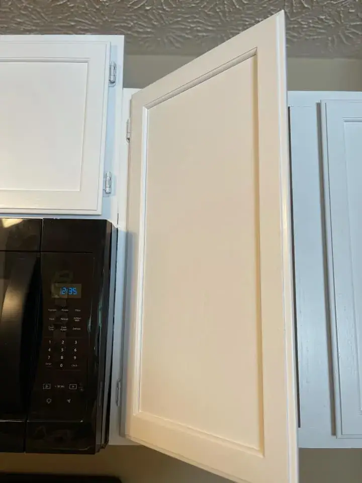 A white kitchen cabinet door standing open next to a black microwave. - My Personal Painter - My Personal Painter After: oak kitchen cabinets painted white