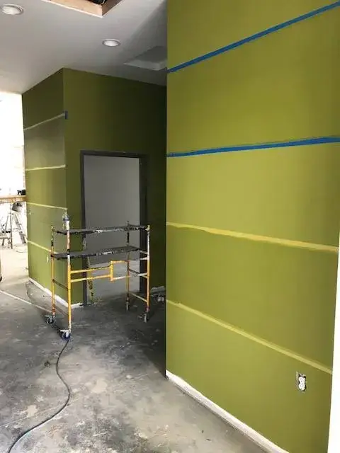 Olive green walls under renovation with horizontal blue painters tape and a rolling metal scaffold. - My Personal Painter - My Personal Painter In progress: olive and charcoal striped commercial walls