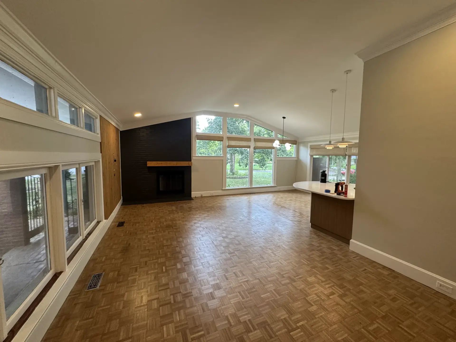 Open living room with fresh beige walls, a dark painted brick fireplace and parquet floors
