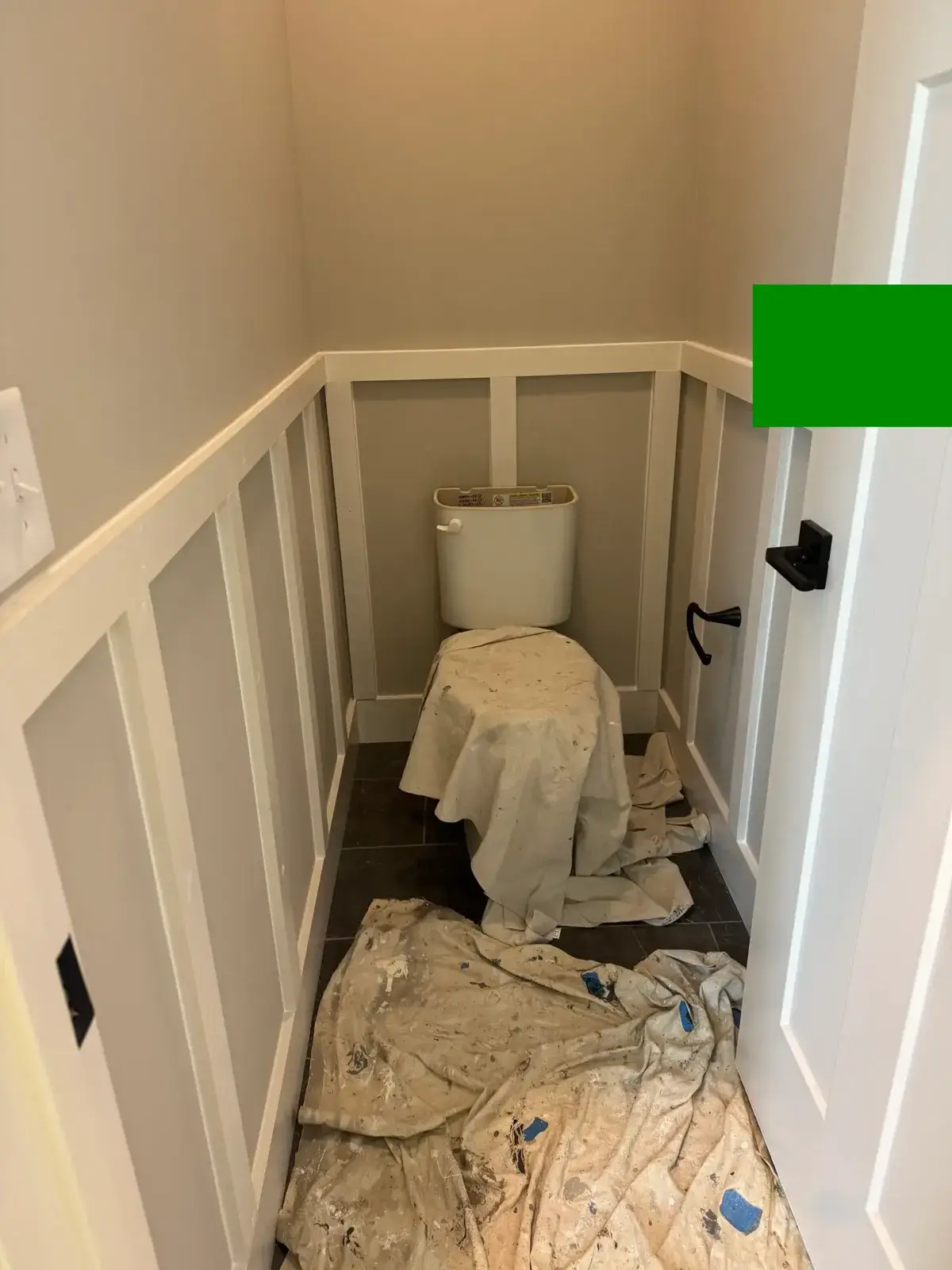 Small bathroom with board and batten walls, a toilet covered by a drop cloth, and a drop cloth on the floor. - My Personal Painter - My Personal Painter In progress: powder room ceiling painted dark brown, bathroom wainscoting and green walls