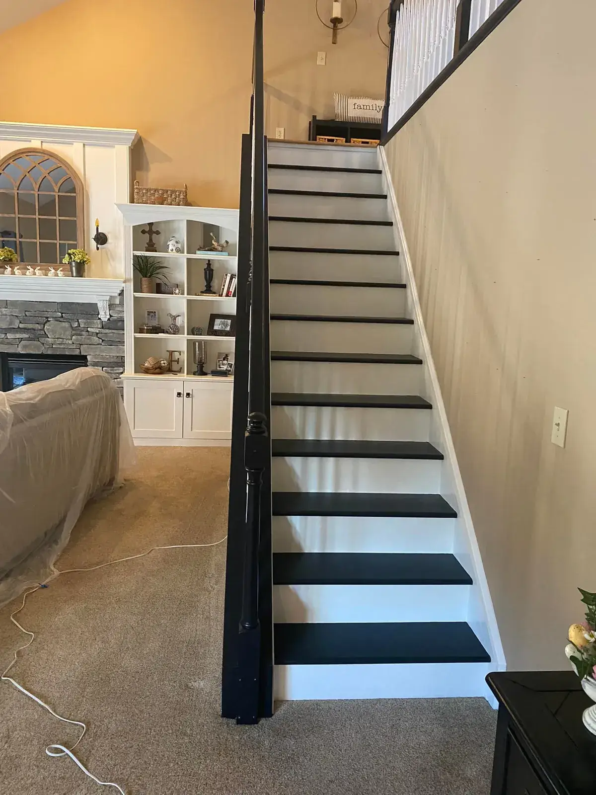 Staircase with black treads and white risers next to a living room with a fireplace and white built-in shelving. - My Personal Painter - My Personal Painter After: staircase: oak railing painted black with white spindles and black treads