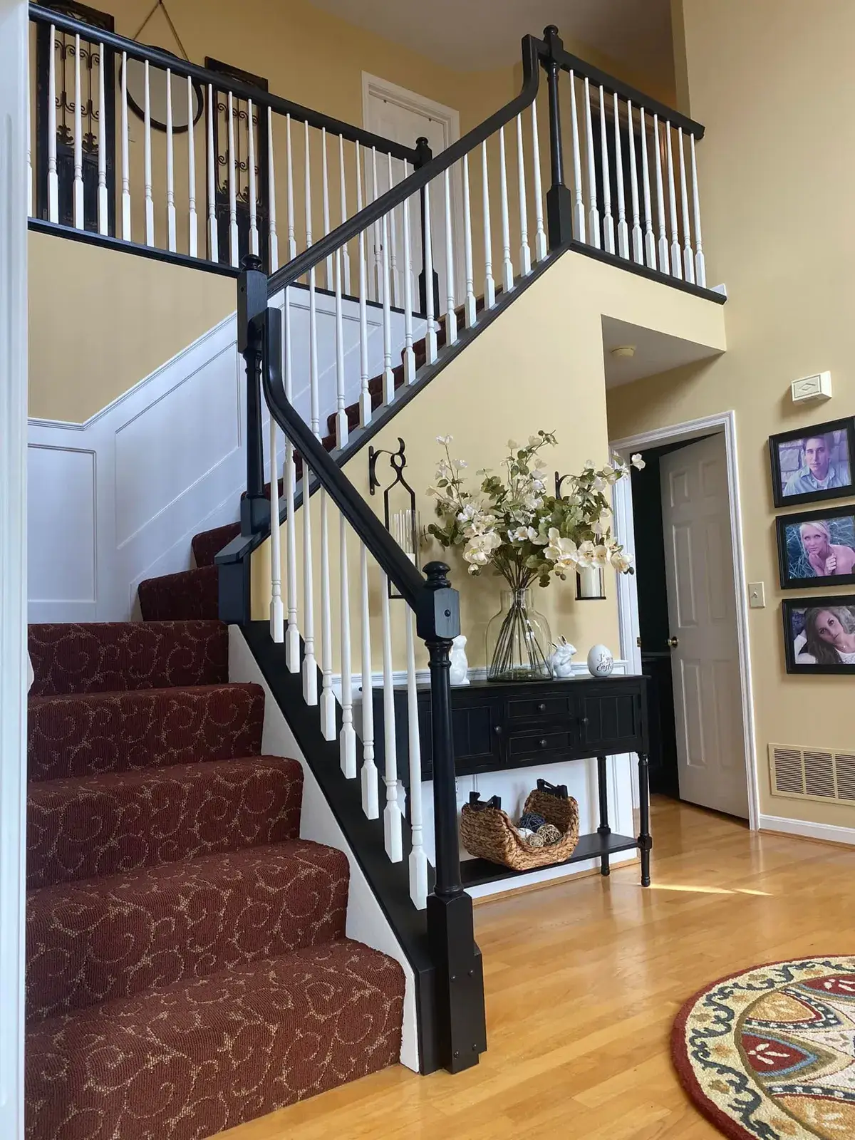 Staircase with patterned red carpet, black railings, and a console table decorated with a floral arrangement. - My Personal Painter - My Personal Painter After: staircase: oak railing painted black with white spindles and black treads