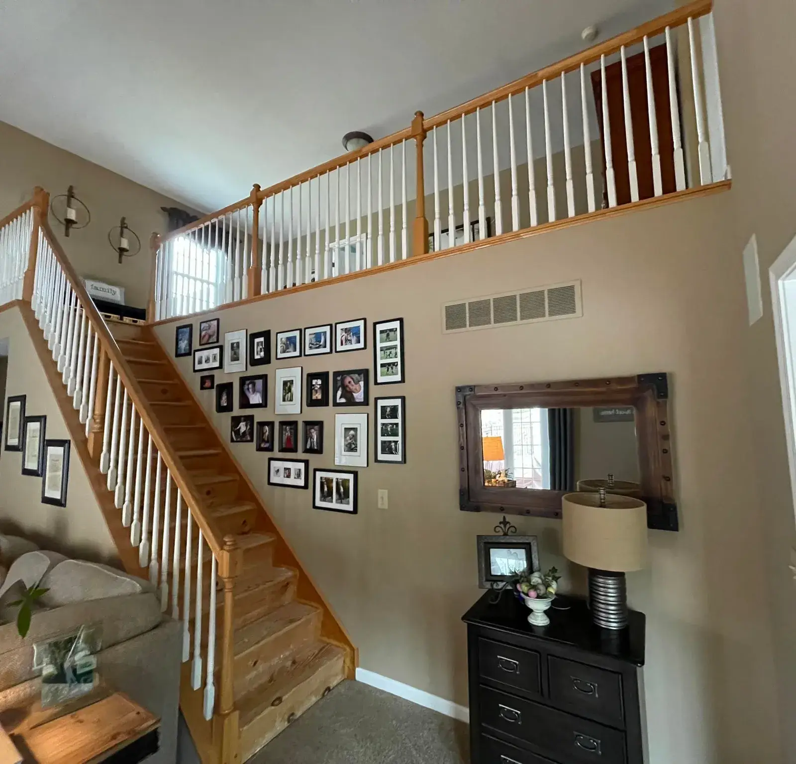 Wooden staircase with a gallery wall of framed photos, a small chest of drawers, and a mirror below a loft railing. - My Personal Painter - My Personal Painter Before: staircase: oak railing painted black with white spindles and black treads