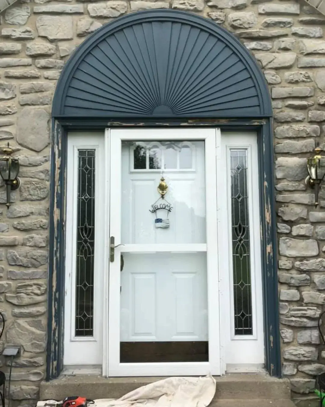 After: stone and brick Cape Cod: front door, arched sunburst and shutters painted dark blue
