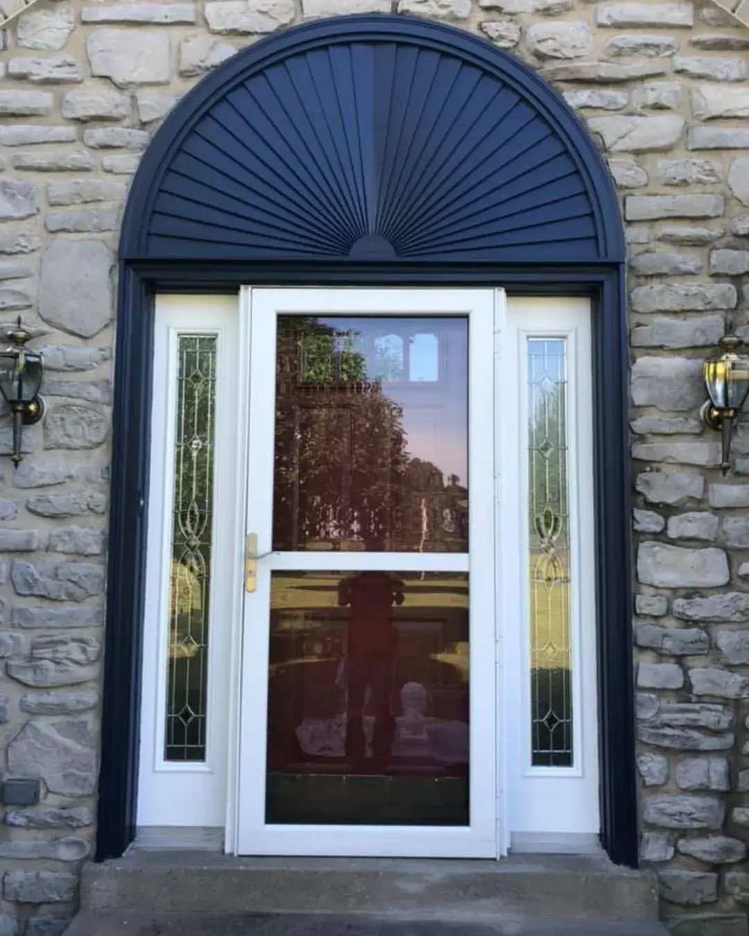 After: stone and brick Cape Cod: front door, arched sunburst and shutters painted dark blue