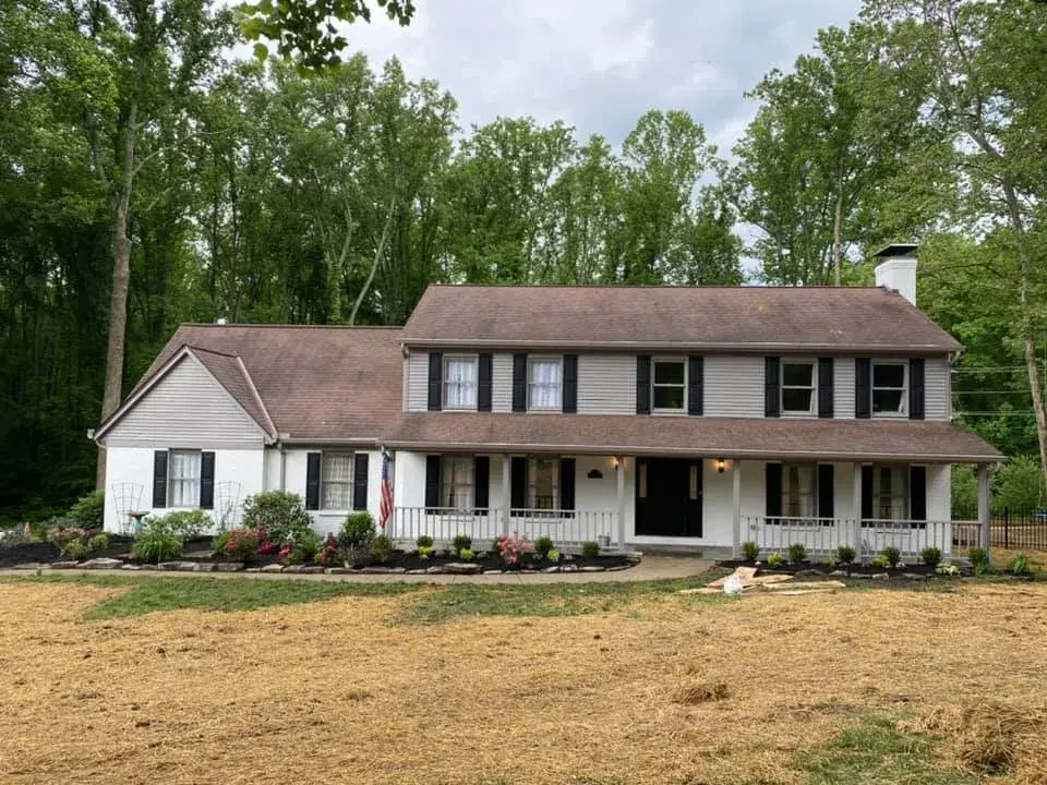 Two-story colonial house with white siding, black shutters, and a front porch, surrounded by trees. - My Personal Painter - My Personal Painter After: two-story brick and siding house painted, red shutters to black