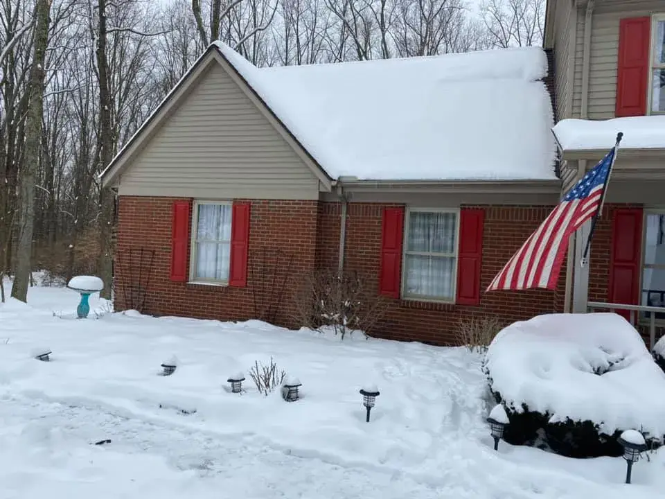 A brick house with red shutters and a snow-covered roof, with an American flag by the front porch. - My Personal Painter - My Personal Painter Before: two-story brick and siding house painted, red shutters to black