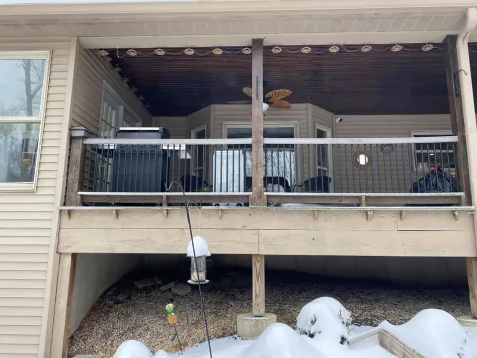 A snow-covered backyard deck with a grill and patio furniture, viewed from below. - My Personal Painter - My Personal Painter Before: two-story brick and siding house painted, red shutters to black