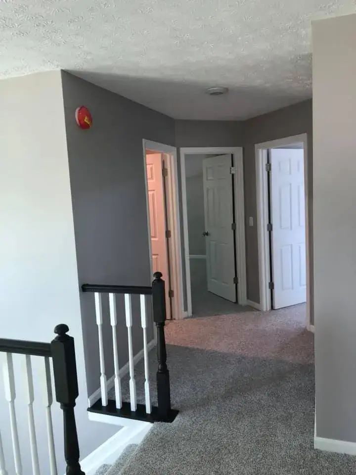 A gray hallway with three open doorways and a staircase railing in the foreground. - My Personal Painter - My Personal Painter After: two-story foyer and rooms painted gray, stair railing painted black