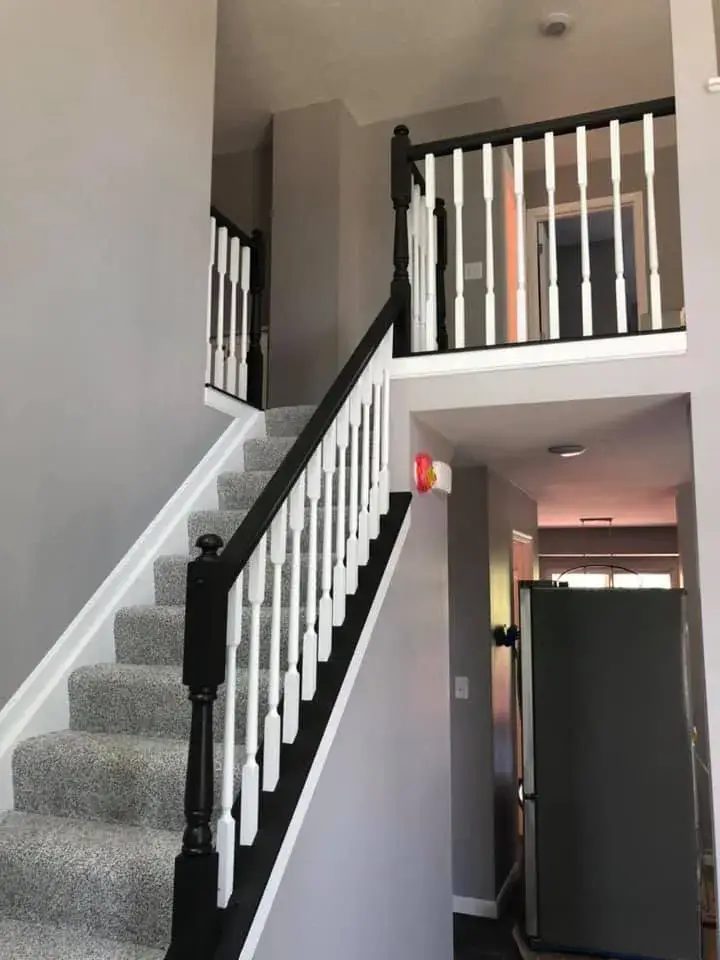 A staircase with gray carpet and black-and-white railings leading to an upper landing. - My Personal Painter - My Personal Painter After: two-story foyer and rooms painted gray, stair railing painted black
