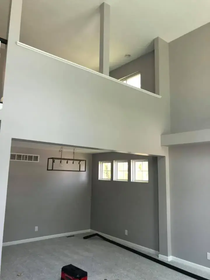 Open-concept room with light gray walls, a linear chandelier, and an overlooking loft space. - My Personal Painter - My Personal Painter After: two-story foyer and rooms painted gray, stair railing painted black