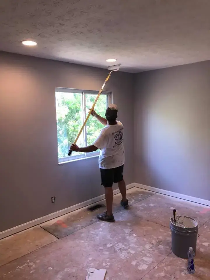 A worker using an extension pole to paint the ceiling of a gray room. - My Personal Painter - My Personal Painter In progress: two-story foyer and rooms painted gray, stair railing painted black