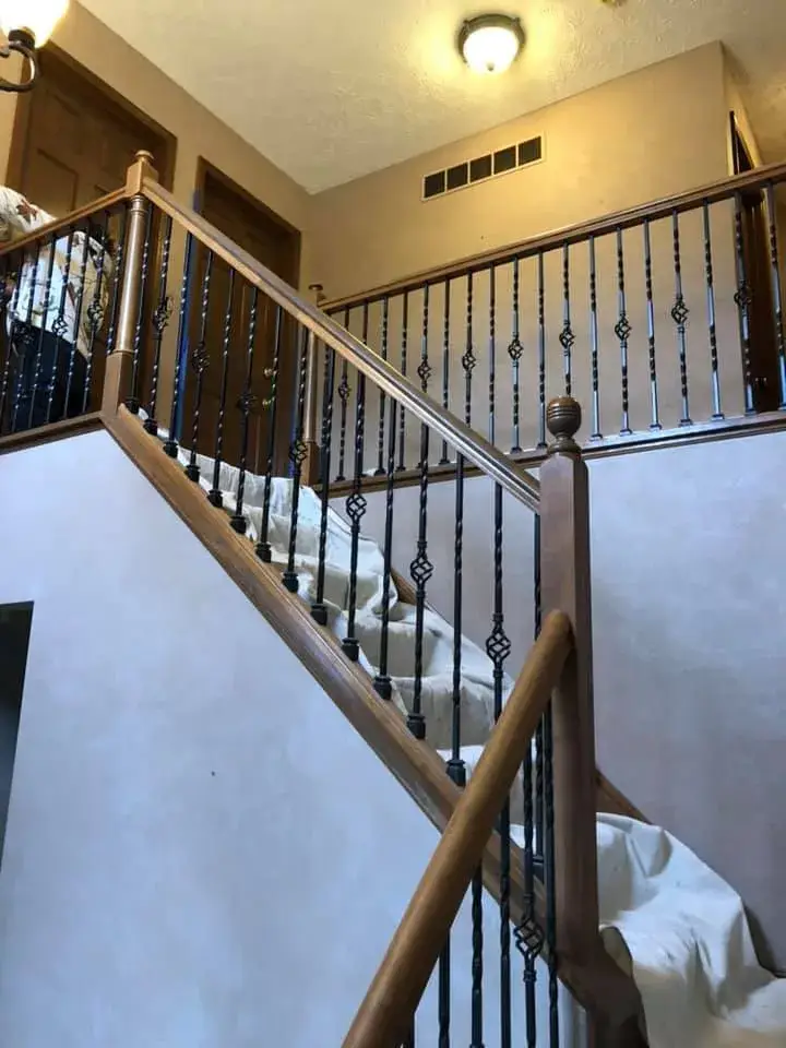 Wooden staircase with black metal balusters, covered with a drop cloth. - My Personal Painter - My Personal Painter In progress: two-story foyer with iron balusters painted