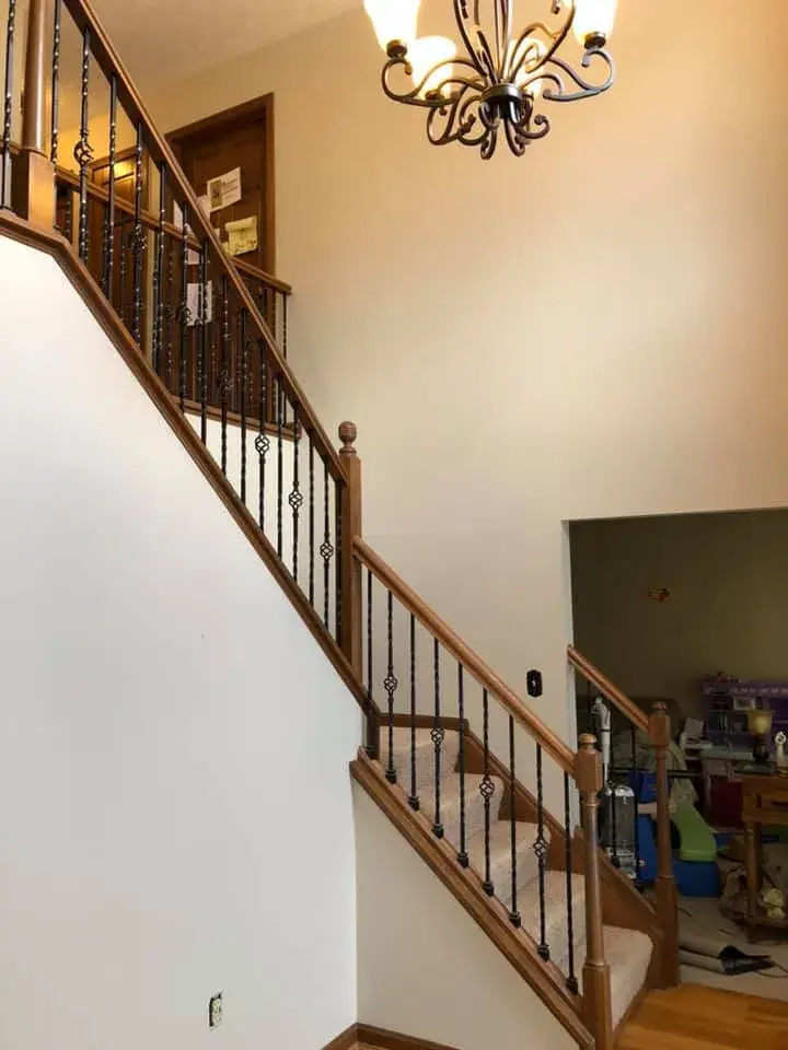 Staircase with wooden handrails and decorative black metal balusters under a traditional chandelier. - My Personal Painter - My Personal Painter In progress: two-story foyer with iron balusters painted