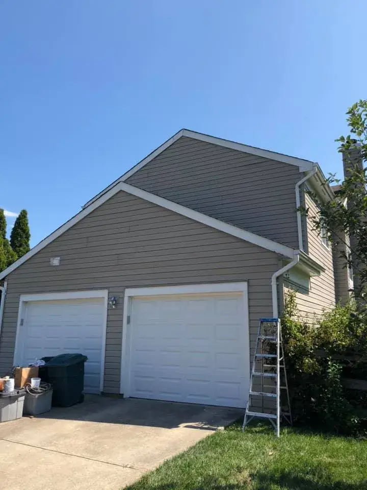 Two-story house with a double garage and a ladder leaning against the side. - My Personal Painter - My Personal Painter In progress: two-story tan siding home exterior trim
