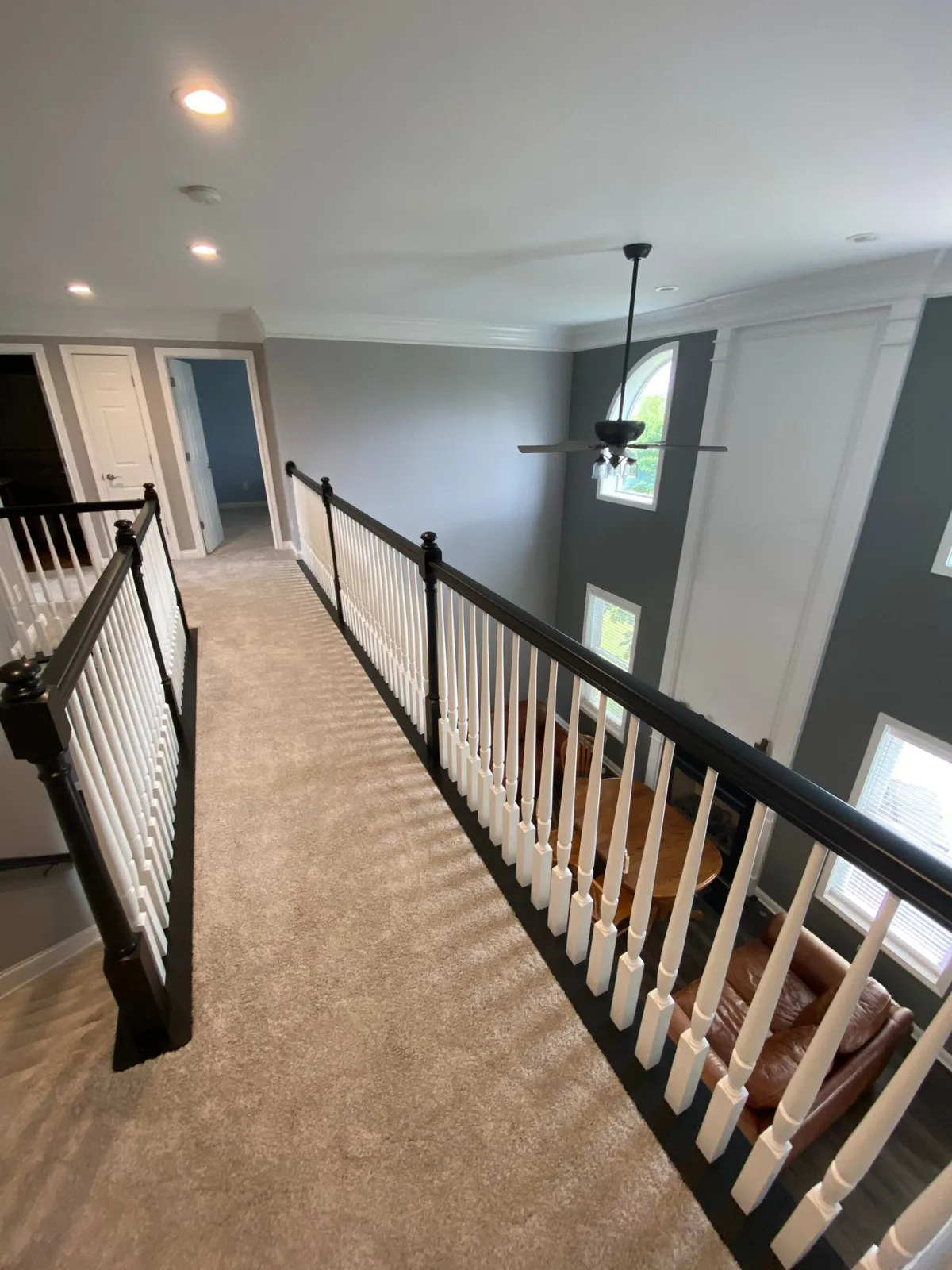 A carpeted hallway overlooking a living room with a dining table and armchair below. - My Personal Painter - My Personal Painter After: upstairs railing painted: black handrail, white spindles
