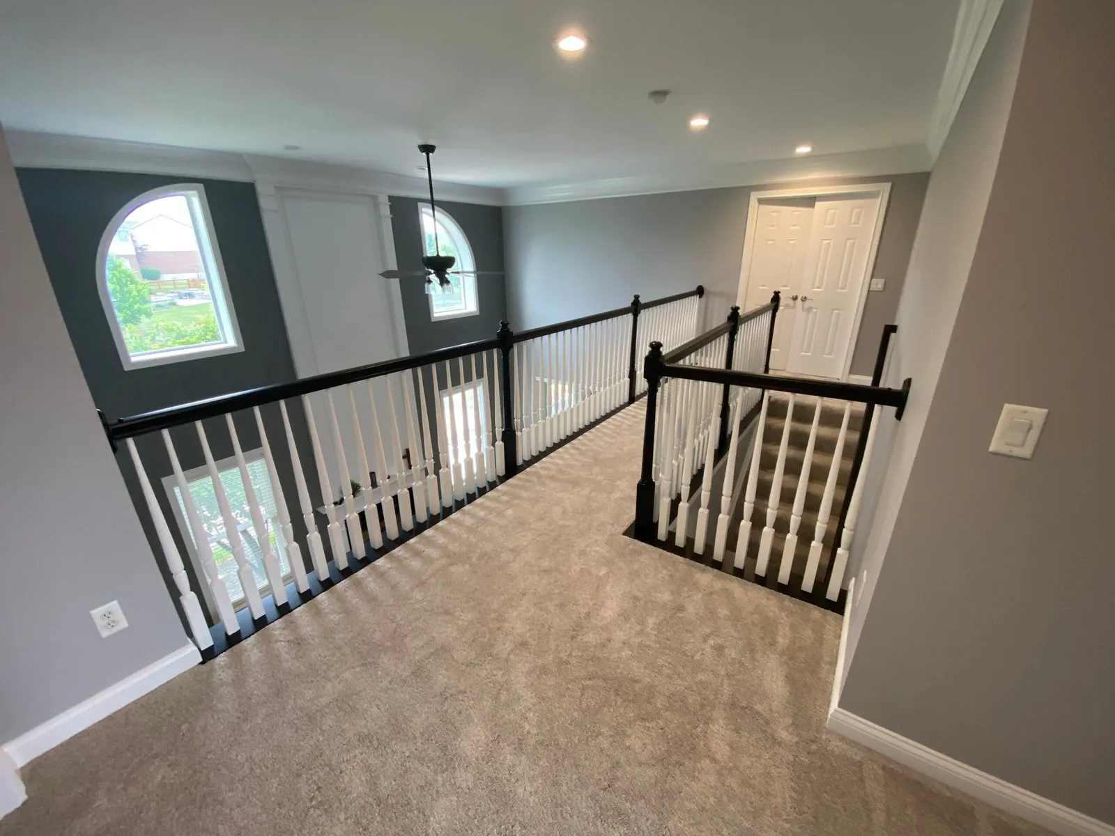 A carpeted hallway with black and white railings overlooking a two-story entryway with arched windows. - My Personal Painter - My Personal Painter After: upstairs railing painted: black handrail, white spindles