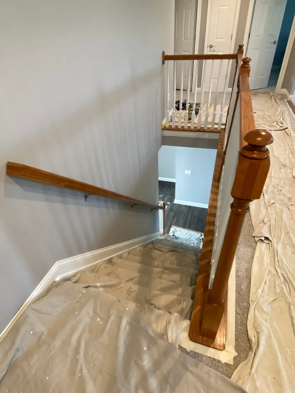 Staircase under renovation with drop cloths covering the steps and floor. - My Personal Painter - My Personal Painter Before: upstairs railing painted: black handrail, white spindles