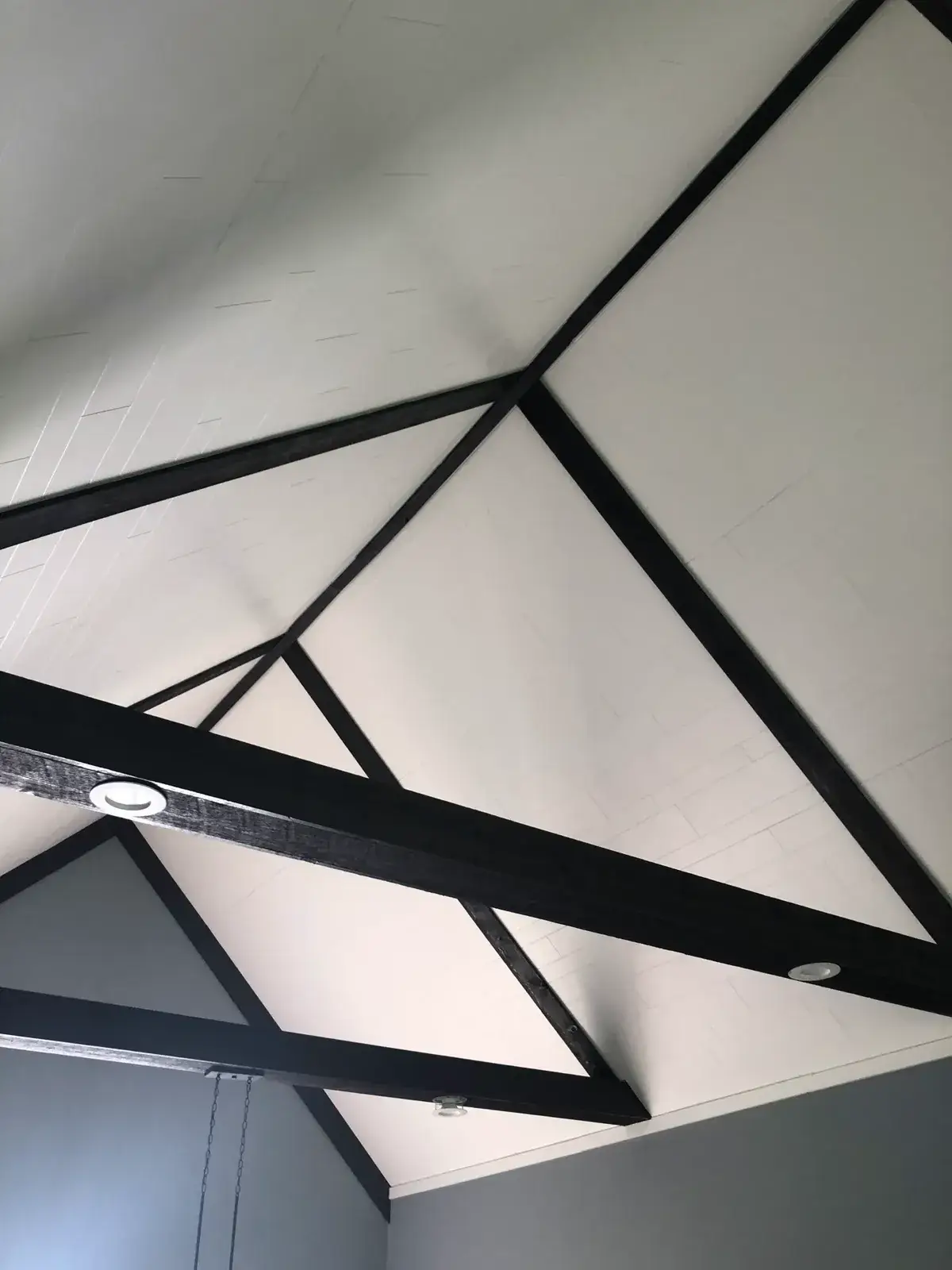 A vaulted white ceiling accented with dark wooden beams and recessed lighting. - My Personal Painter - My Personal Painter After: vaulted great room: brick chimney painted, then stained wood ceiling to white planks and black beams