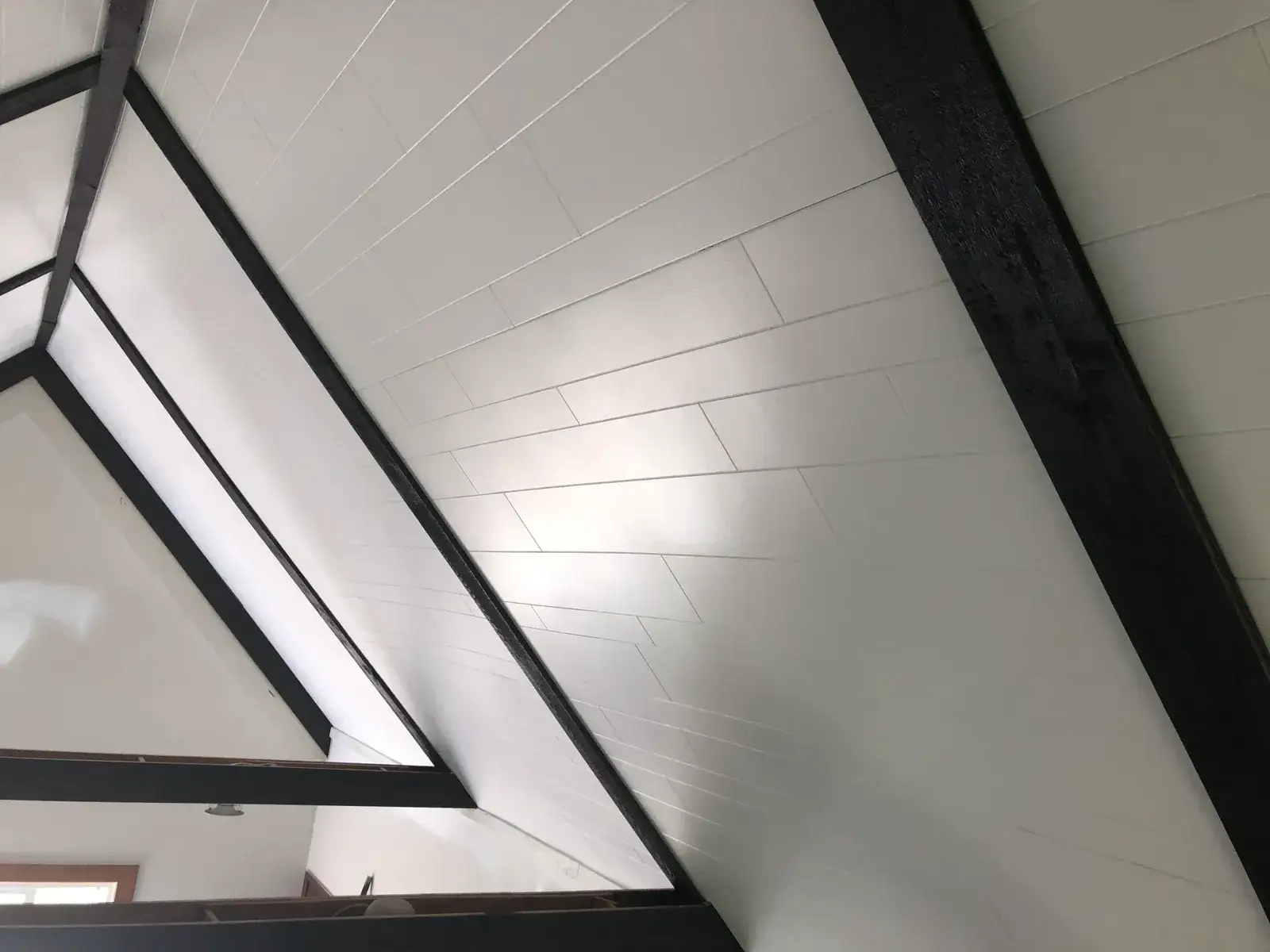 White paneled ceiling with dark exposed structural beams in an A-frame room. - My Personal Painter - My Personal Painter After: vaulted great room: brick chimney painted, then stained wood ceiling to white planks and black beams