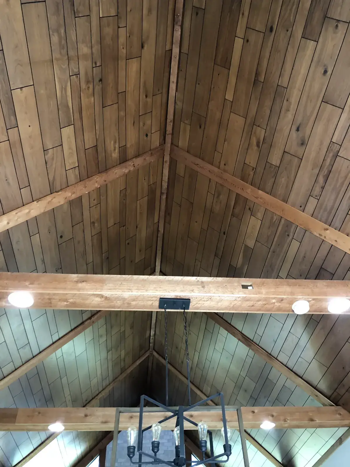 A vaulted wood-paneled ceiling with exposed beams and a hanging black metal chandelier. - My Personal Painter - My Personal Painter Before: vaulted great room: brick chimney painted, then stained wood ceiling to white planks and black beams