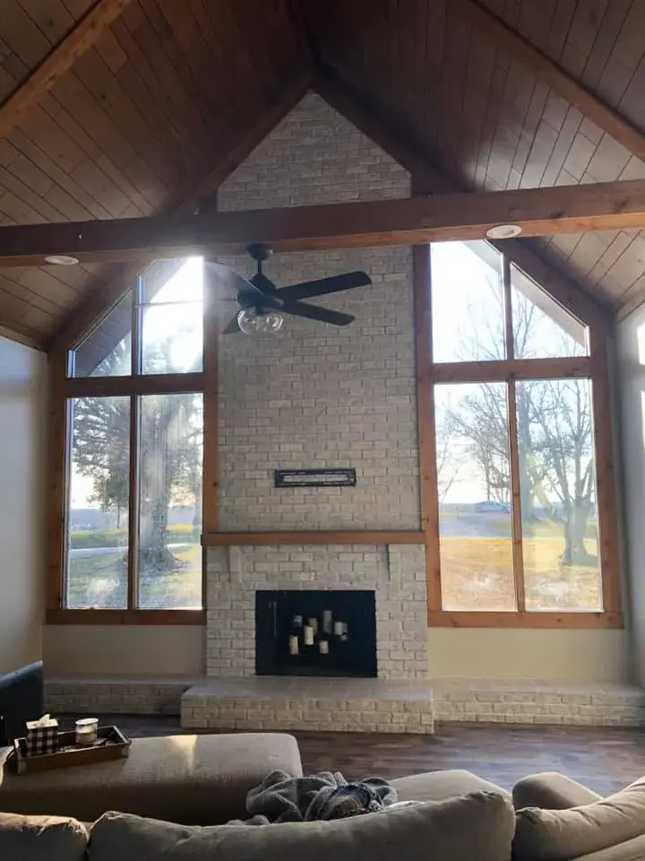 A brick fireplace with a mantel sits between two tall windows under a vaulted wooden ceiling. - My Personal Painter - My Personal Painter In progress: vaulted great room: brick chimney painted, then stained wood ceiling to white planks and black beams