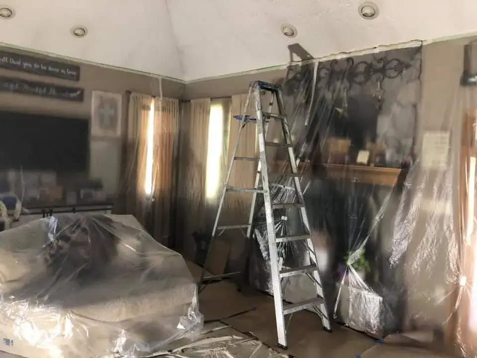 A living room prepared for painting with plastic drop cloths covering the furniture, walls, and a ladder standing in center. - My Personal Painter - My Personal Painter In progress: vaulted living room, stairwell and textured ceilings painted