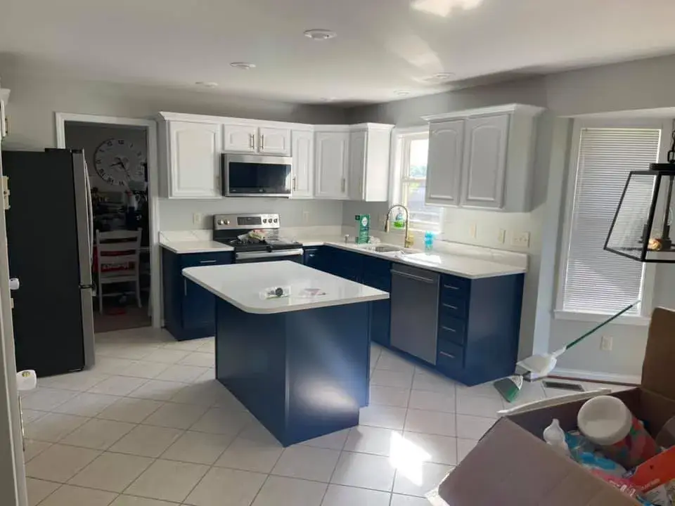 Kitchen with a dark blue island and lower cabinets, white upper cabinets, and white countertops. - My Personal Painter - My Personal Painter After: wood kitchen painted white with navy island