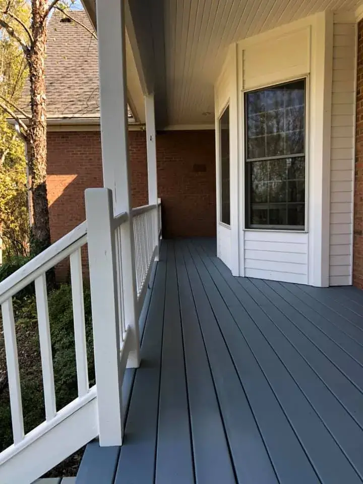 A gray deck with white railings wraps around the corner of a brick house. - My Personal Painter - My Personal Painter After: wraparound porch on brick Cape Cod: railings white, floor painted blue-gray