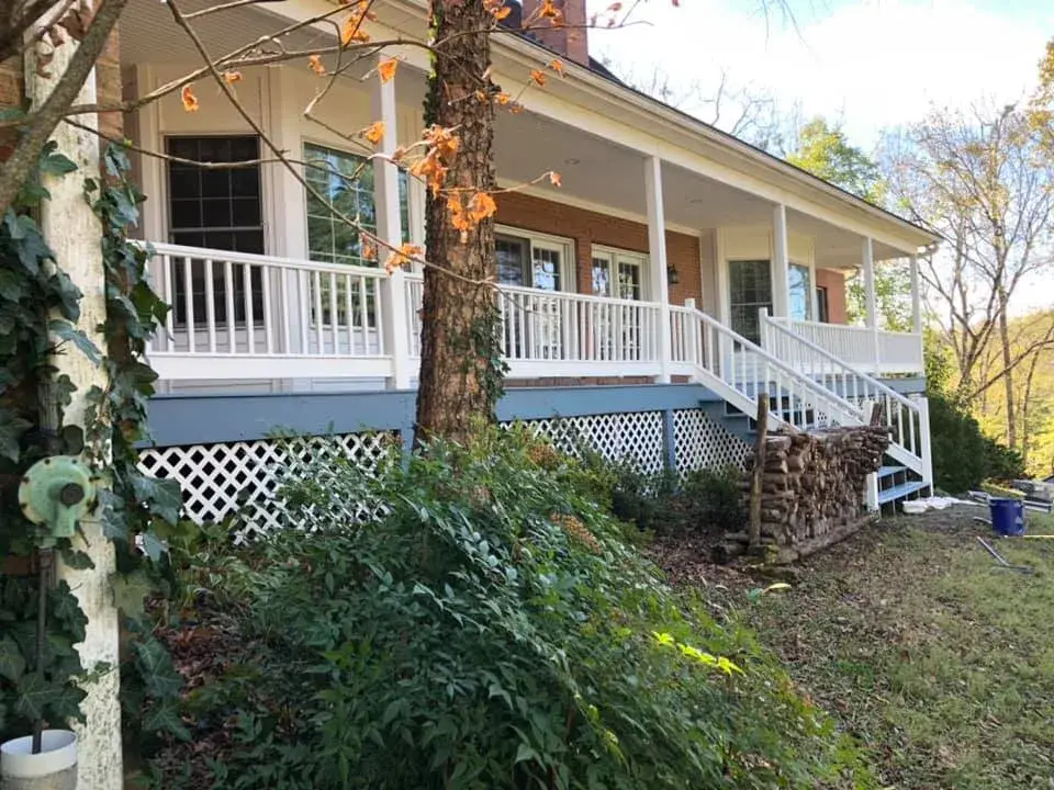 A brick house with a wide front porch, white railings, and a stack of firewood nearby. - My Personal Painter - My Personal Painter After: wraparound porch on brick Cape Cod: railings white, floor painted blue-gray