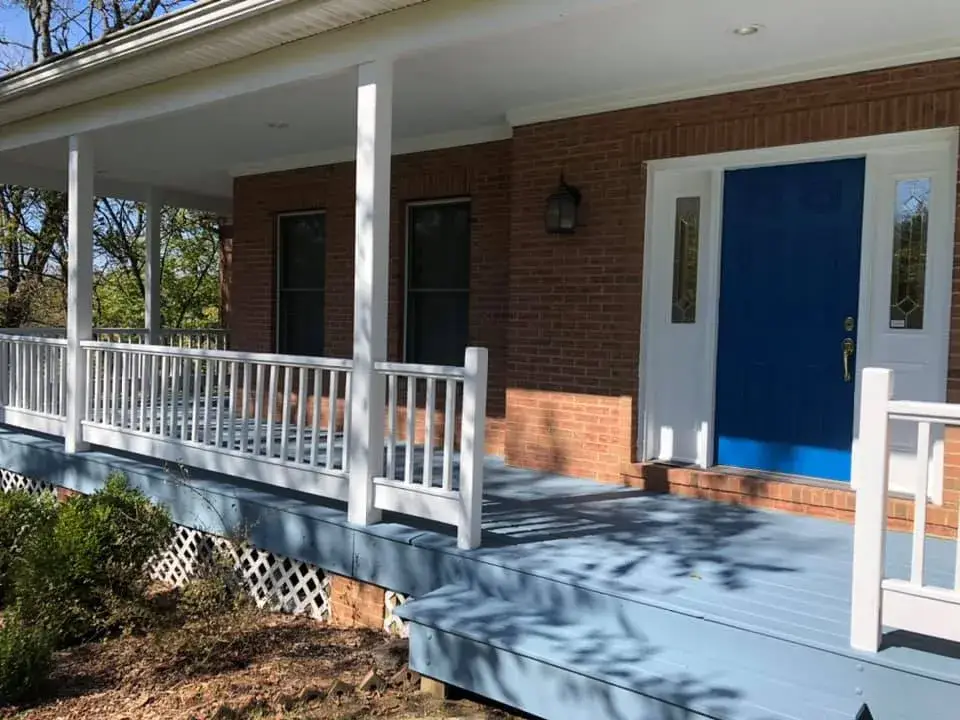 A brick house with a blue front door and a wide front porch with white railings. - My Personal Painter - My Personal Painter After: wraparound porch on brick Cape Cod: railings white, floor painted blue-gray